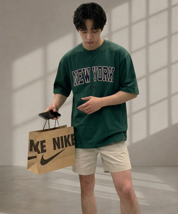 ダークグリーンのNEW YORKロゴTシャツにベージュのハーフパンツを合わせた男性の正面からのコーディネート