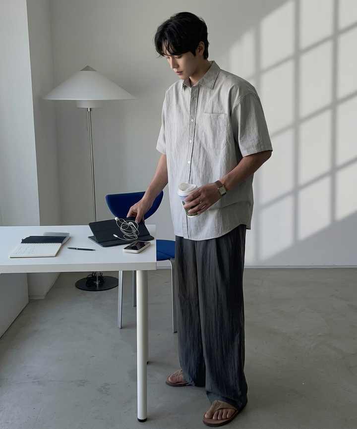 グレーの半袖シャツとダークグレーのワイドパンツを合わせ、コーヒーカップを持って立つ男性の全身カット