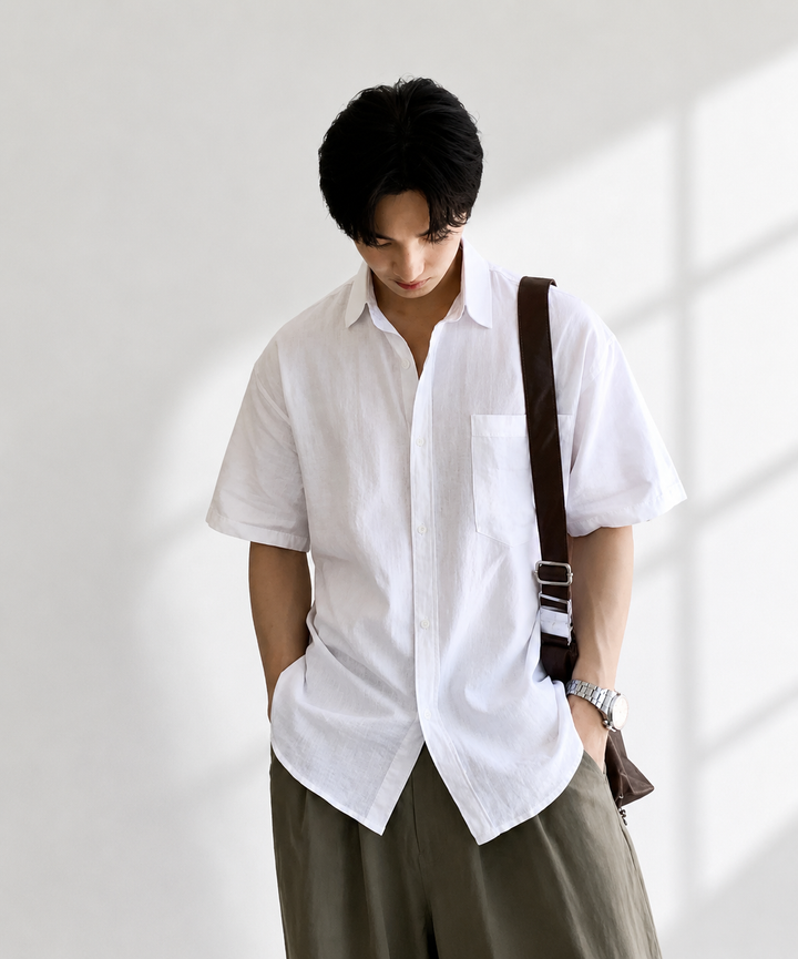 ホワイトのリネン半袖シャツにカーキのパンツを合わせ、両手をポケットに入れて立つ男性の正面カット。
