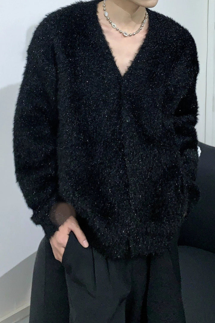 ラメ入りのブラックのシャギーニットカーディガンを着用し、片手をパンツのポケットに入れた男性の左斜めからのカット。