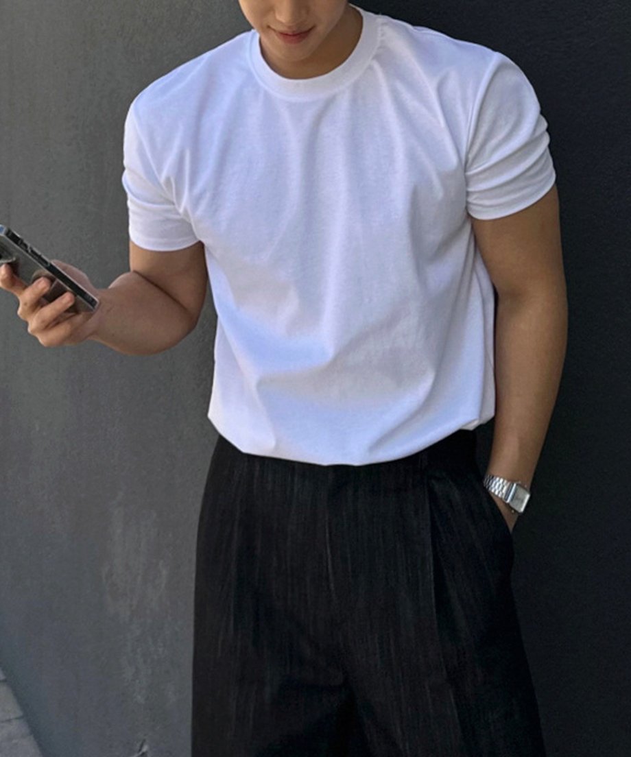白い半袖クルーネックTシャツを黒いスラックスにタックインし、左手に腕時計をつけてスマートフォンを持つ男性の斜め前からの上半身ショット。