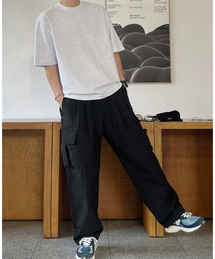 フラワーグレーの半袖Tシャツにブラックのワイドカーゴパンツ、ブルーとホワイトのコンビスニーカーを合わせ、片手をポケットに入れてポーズをとる男性の正面全身スタイリング。