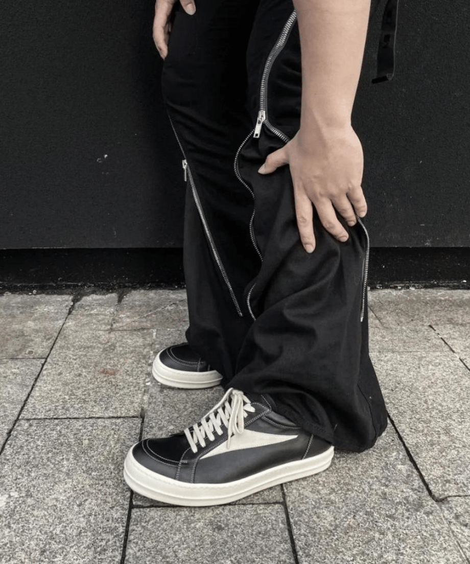サイドにジッパーデザインが施された黒のワイドパンツに、黒の厚底レザースニーカーを合わせたスタイリングカット。