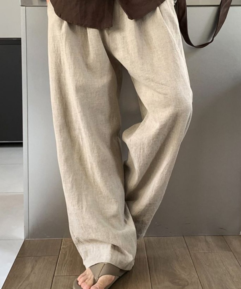 コーヒー色のシャツの下に、フラワーベージュのツータックワイドパンツを穿いた男性の正面からの立ち姿。