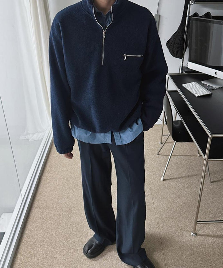 ネイビーのハーフジップフリースのインナーにブルーのシャツを重ね着し、裾からシャツを覗かせた男性のスタイリッシュなコーディネート。