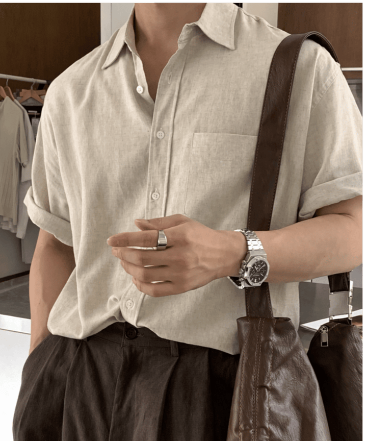 ベージュのリネン半袖シャツにブラウンのパンツを合わせ、茶色のレザーバッグを肩に掛けた男性のチェストアップ。