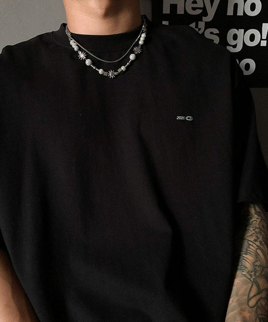 黒のタートルネックTシャツを着用した男性の首元に、シルバーチェーンとパール調ビーズ、そして太陽（フラワー）モチーフが美しく重なるスタイリッシュな着用カット。