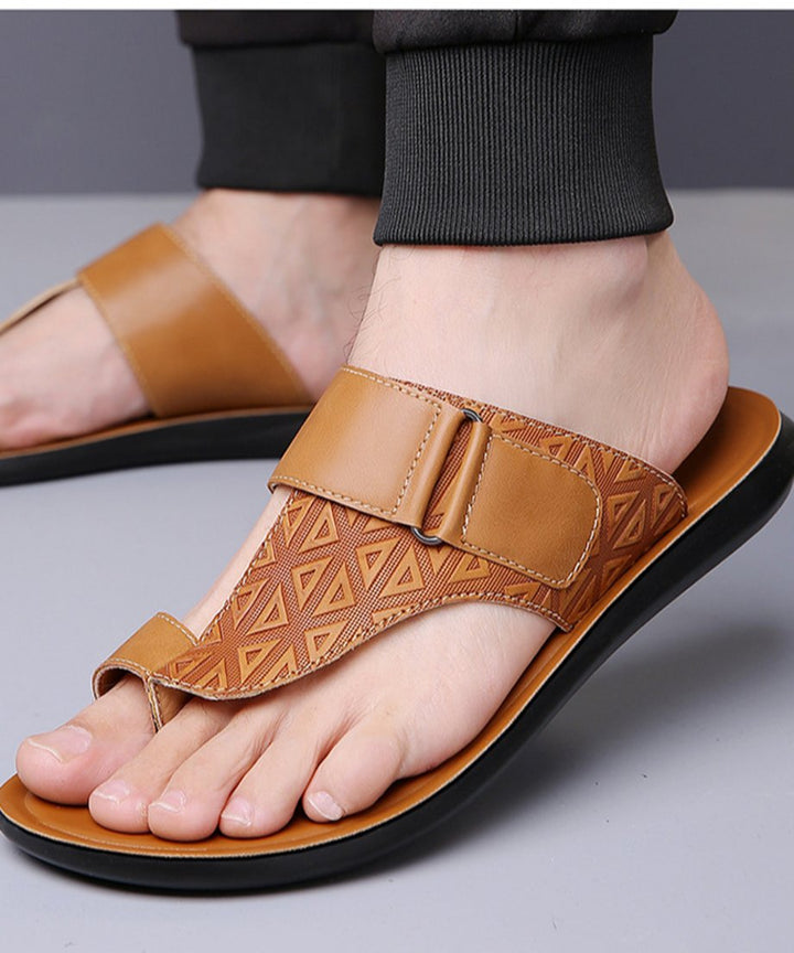 グレーの背景で、黒い裾絞りのパンツを穿いた男性がブラウンのトングサンダルを着用している足元のカット。