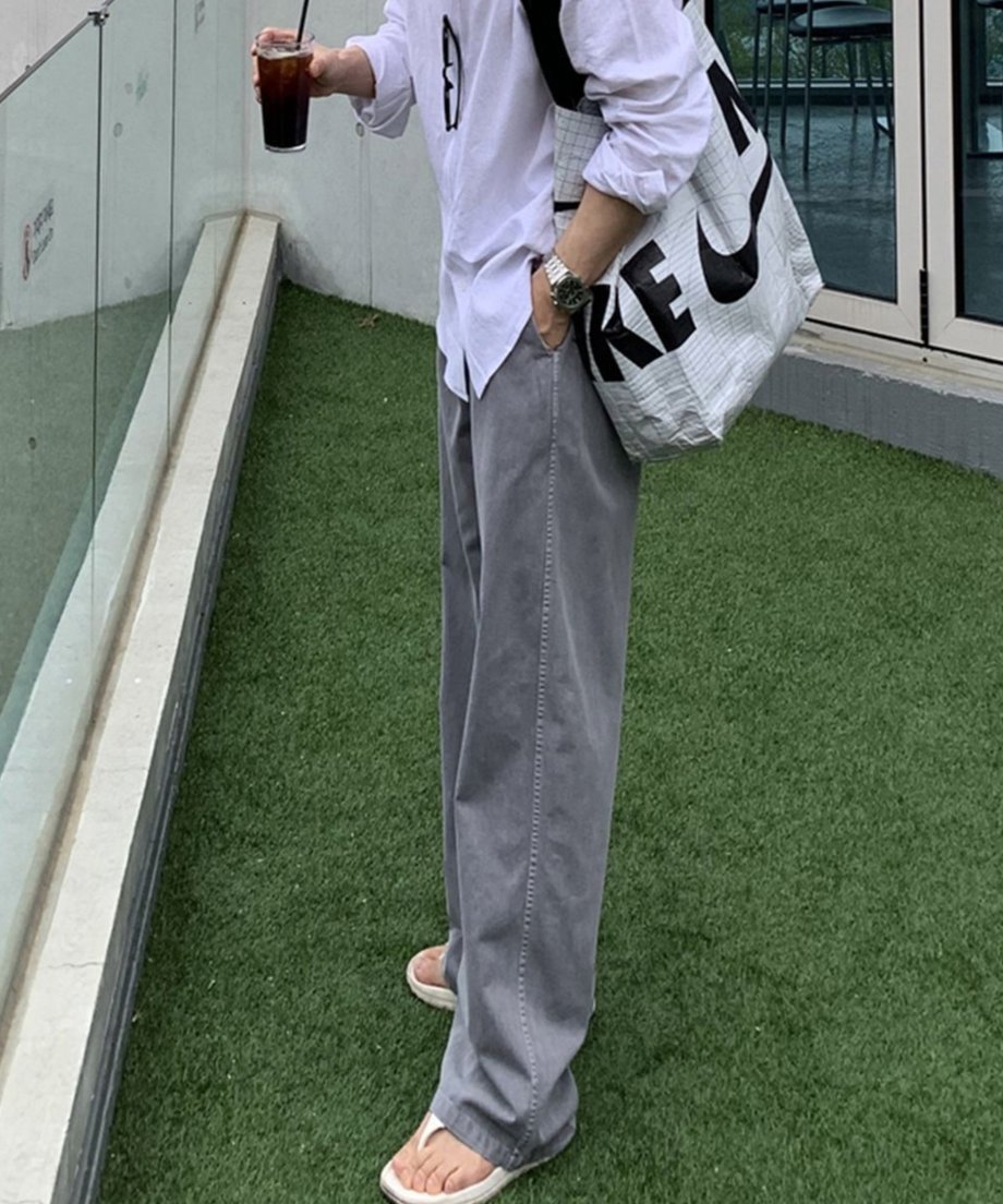 屋外の人工芝の上で、白の長袖リネンシャツにライトグレーのピグメントイージーワイドパンツ、白のトングサンダルを合わせた男性の左側面からのスタイリング写真。