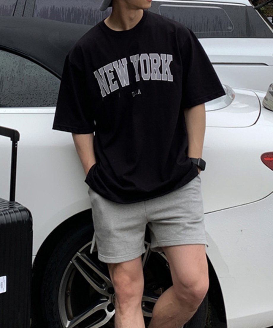 白い車の前でブラックのNEW YORKロゴTシャツとグレーのハーフパンツを着用した男性の正面カット