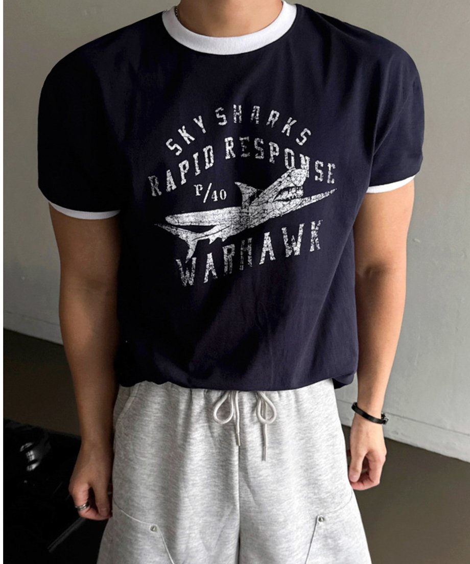 ネイビーのリンガーTシャツとグレーのスウェットショーツを着用し、正面を向いて立つ男性の上半身カット。