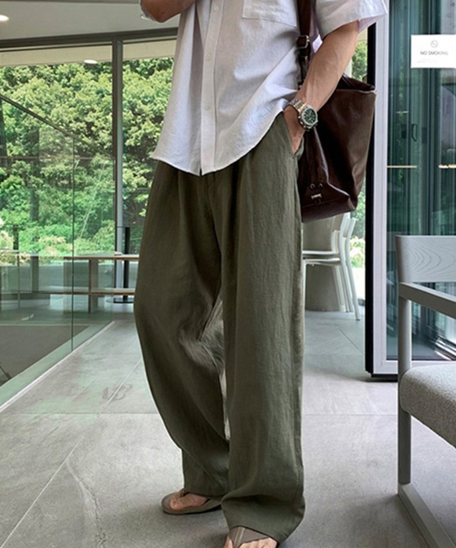白の半袖シャツとアーミーグリーンのツータックワイドパンツを着用し、茶色のレザーバッグを肩に掛けた男性の立ち姿。