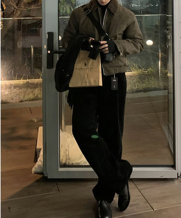 ブラウンのボア襟フライトジャケットに黒のパンツを合わせ、足を交差させてスマートに佇む男性の全身カット。