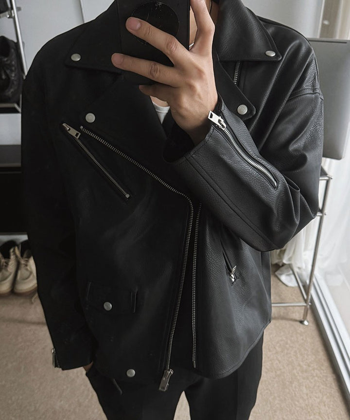 黒のライダースジャケットを着用した男性が、スマートフォンを鏡にかざして自撮り（セルフィー）をしている上半身カット。
