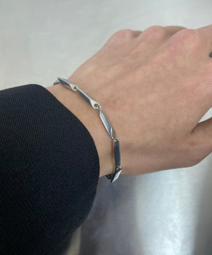 黒いジャケットの袖口から覗く、直線的な多面体メタルリンクブレスレットを着用した男性の手元カット