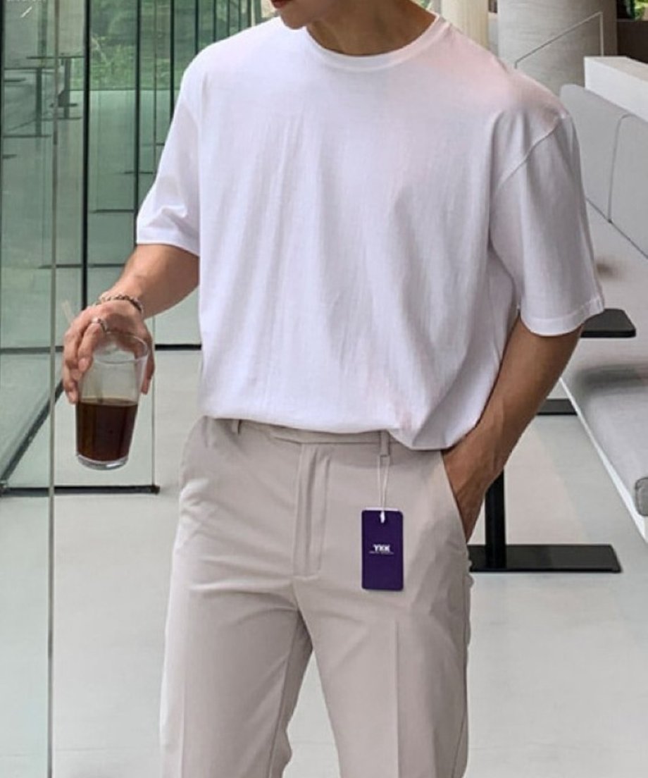 ホワイトのクルーネックTシャツに、ベージュのスラックスを合わせて片手にグラスを持った男性の正面からのカット。