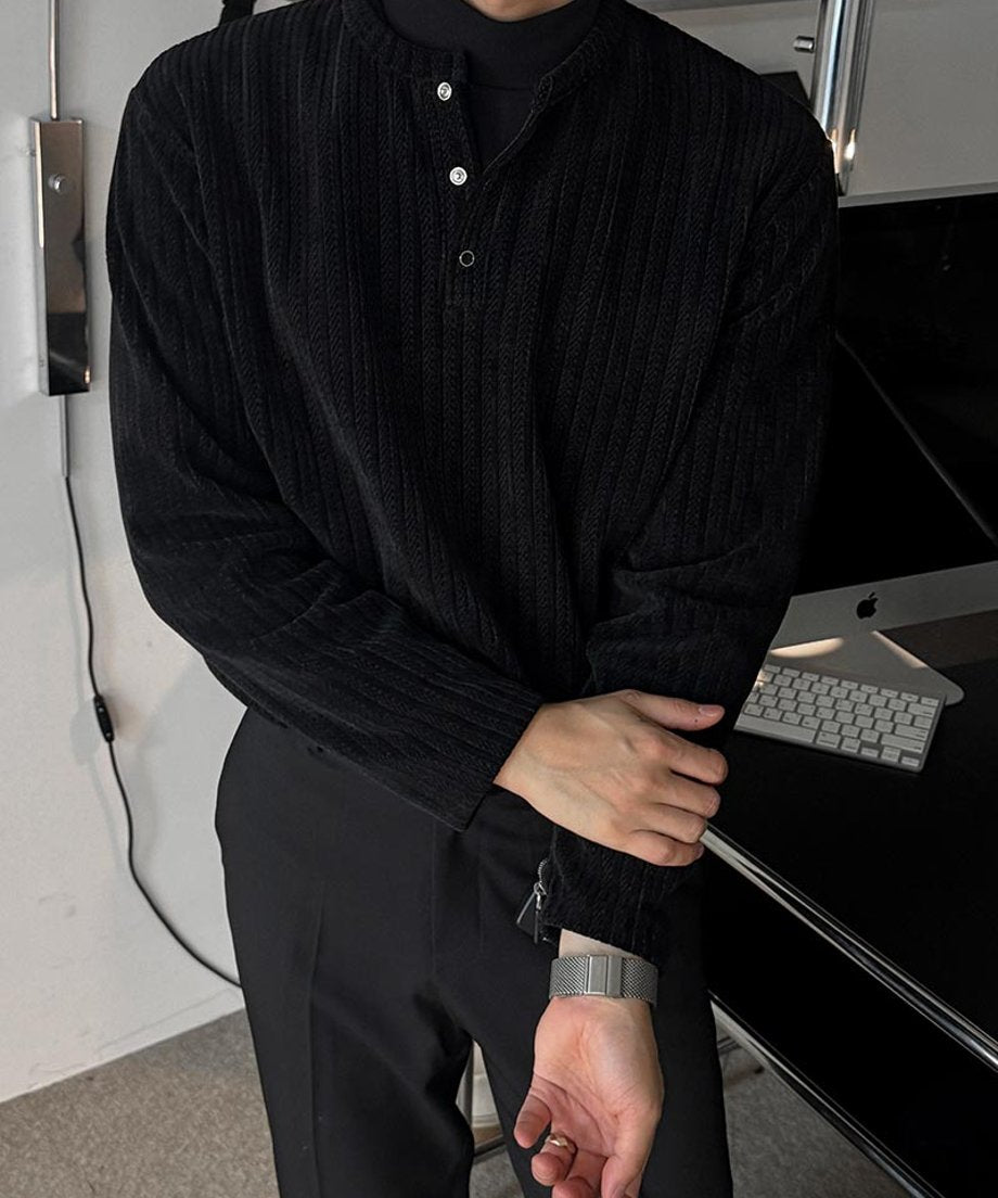 ブラックのリブ編みヘンリーネックカットソーを着用し、黒のスラックスにタックインして腕組みをしている男性のスタイリング写真。