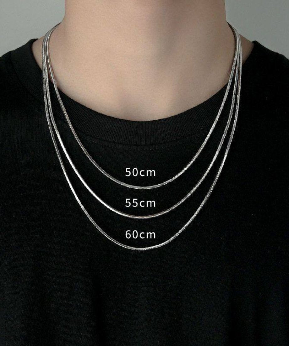 黒クルーネックTシャツを着用した男性の胸元で、50cm、55cm、60cmの3つの異なる長さのスネークチェーンが美しいレイヤードを描くサイズ比較の正面着用カット。