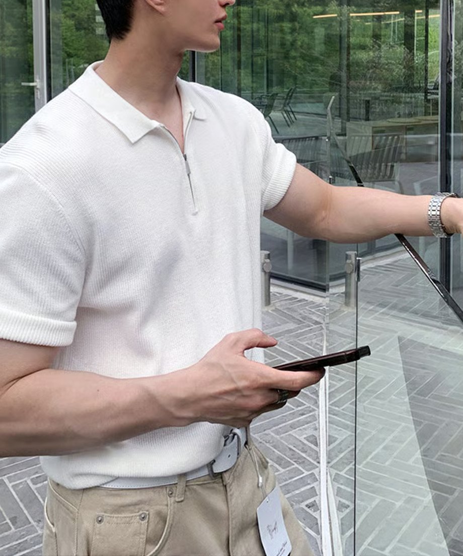 清潔感のあるホワイトのハーフジップニットポロにベージュのデニムパンツを合わせ、スマートフォンを手にする男性のクリーンなカジュアルカット。