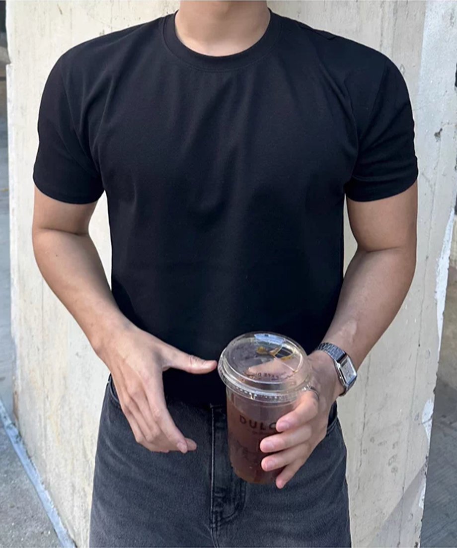 黒い半袖クルーネックTシャツを着用し、両手でプラスチックカップのドリンクを持つ男性の正面からのアップショット。