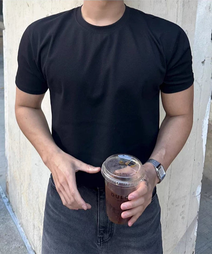 黒い半袖クルーネックTシャツを着用し、両手でプラスチックカップのドリンクを持つ男性の正面からのアップショット。