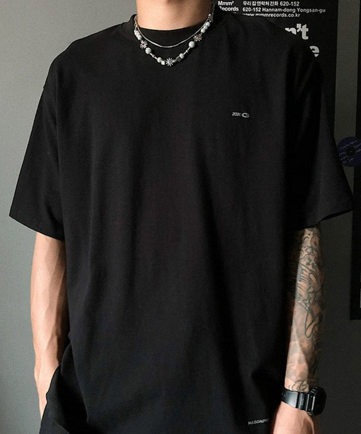 オーバーサイズの黒Tシャツとタトゥーの入った腕元を背景に、アシンメトリーなビーズ配置が際立つネックレスの正面着用スタイリング。