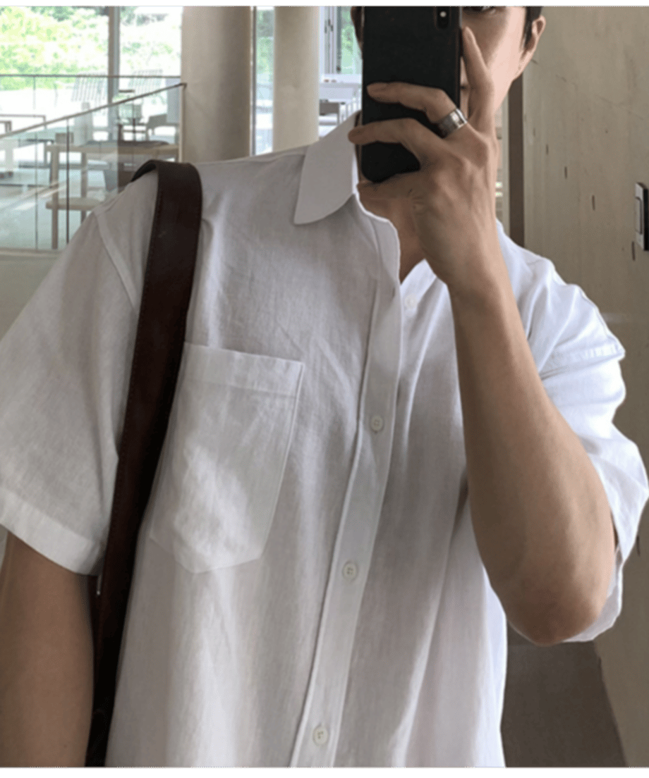 ホワイトのリネン半袖シャツを着用し、スマートフォンで鏡越しに自撮りをする男性の胸元のカット。