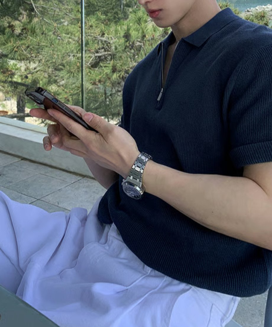 深みのあるネイビーのハーフジップニットポロを着用し、屋外でスマートフォンを見つめる男性の横顔と腕元のアップカット