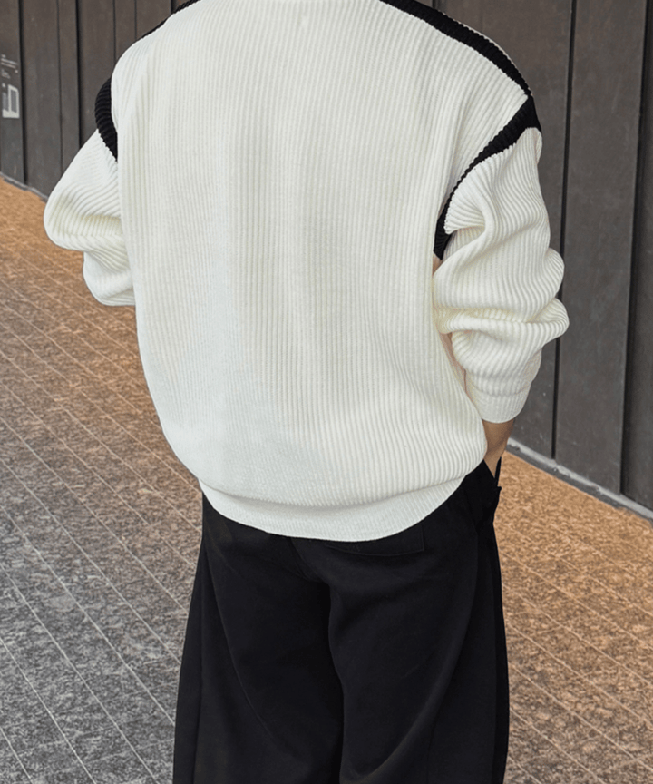 グレーの壁沿いで、ホワイトのリブニットジップジャケットと黒のワイドパンツを着用した男性の後ろ姿。