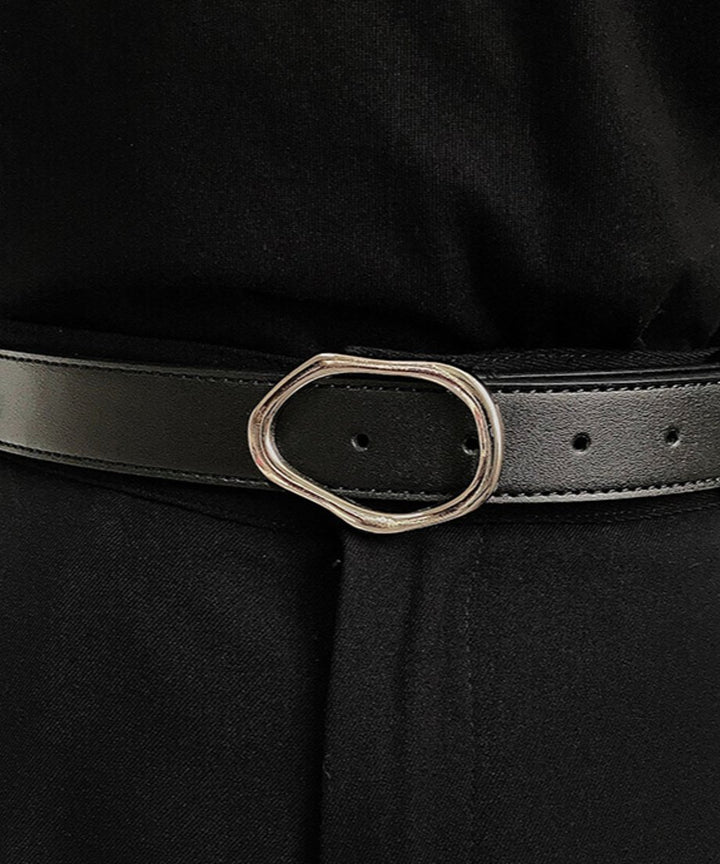 黒いトップスとボトムスを着用した人物の腰元で、シルバーの有機的な形のバックルがアクセントになっているブラックレザーベルトの着用フロントカット。