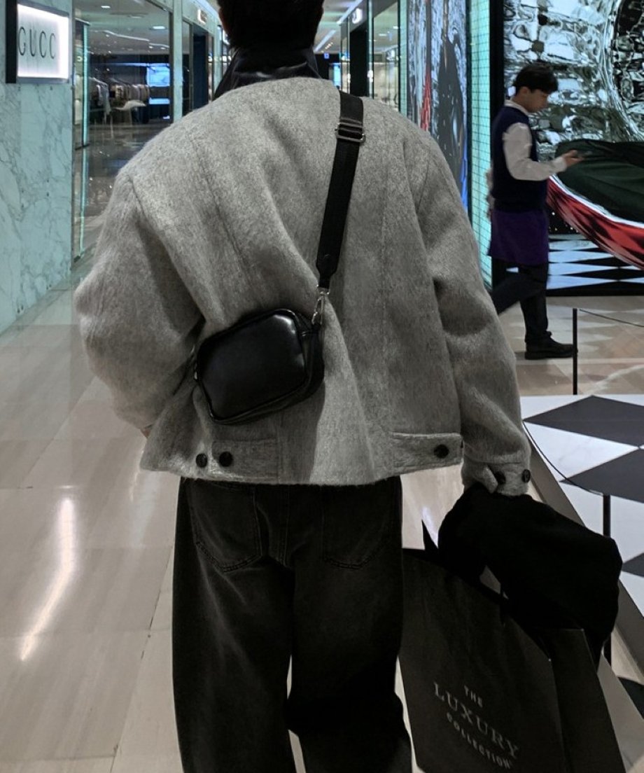 シルバーグレーのジップアップジャケットに黒のミニショルダーバッグを斜め掛けして歩く男性の後ろ姿カット。