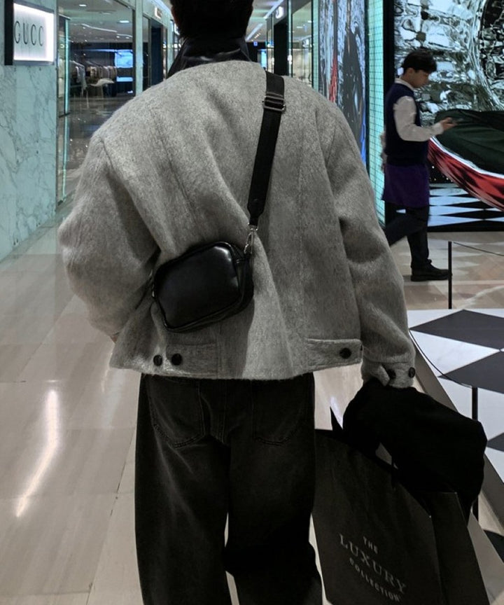 シルバーグレーのジップアップジャケットに黒のミニショルダーバッグを斜め掛けして歩く男性の後ろ姿カット。