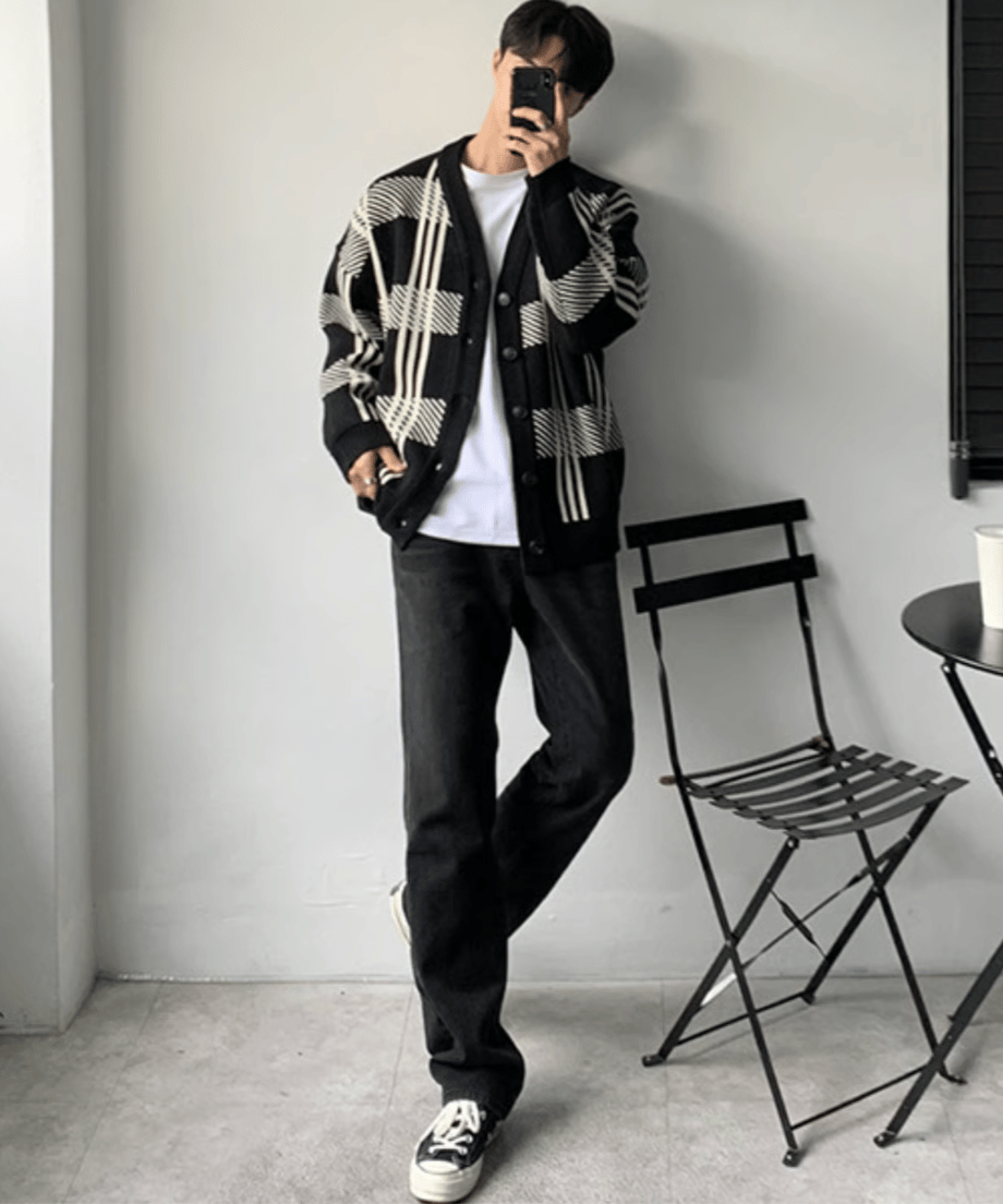 大柄なブラックチェックのVネックニットカーディガンに白Tシャツ、黒のストレートデニム、黒のスニーカーを合わせた男性の全身スタイリングカット。