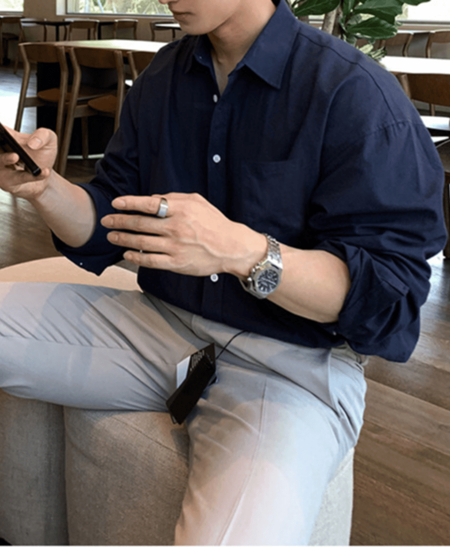 ネイビーの長袖シャツとライトグレーのスラックスを着用し、カフェのスツールに腰掛けてスマートフォンを両手で操作している男性のクローズアップカット。