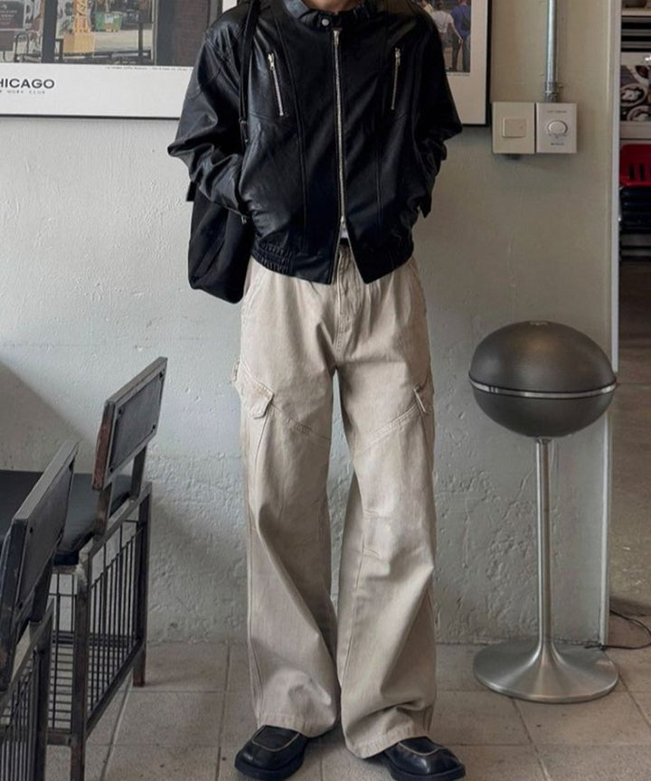 黒のレザージャケットに黒のバッグを背負った人物が、カーキのワイドカーゴパンツを穿いてリラックスした様子で立っている、室内での全身コーディネート写真。