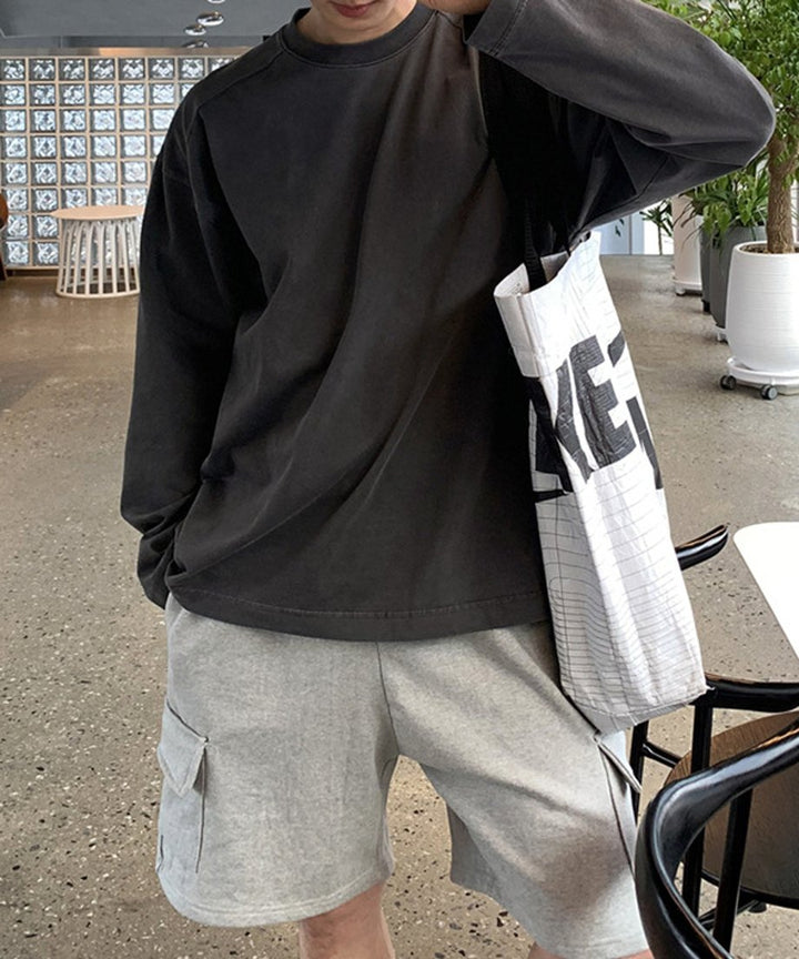 アイアングレーのルーズフィット長袖Tシャツを着用し、大きなモノトーンのロゴ入りトートバッグを肩に掛けた男性のフロントアップカット。