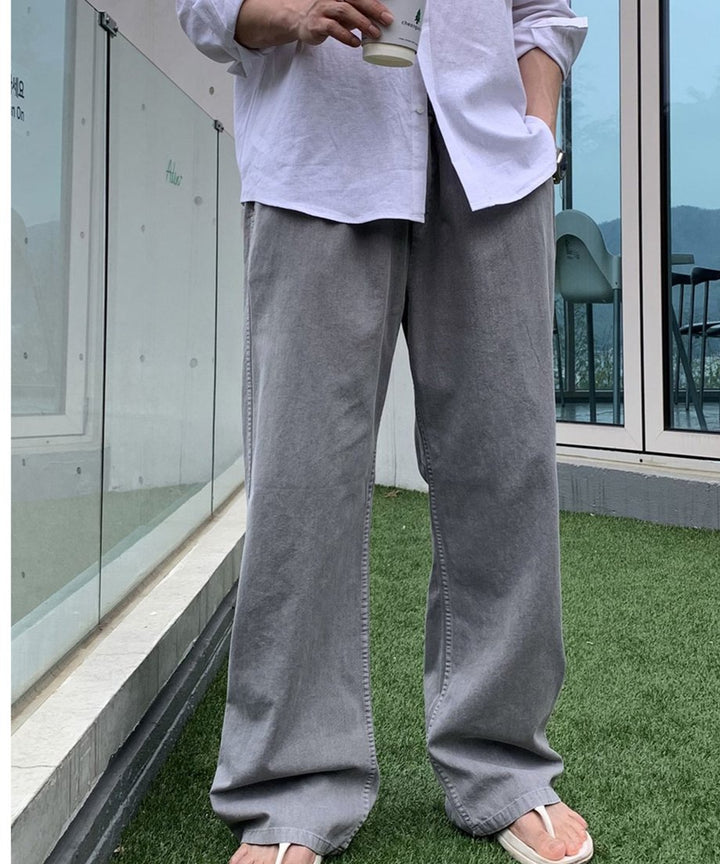 白シャツの裾をラフに出し、ライトグレーのピグメントイージーワイドパンツを穿いた男性の正面からの立ち姿カット。