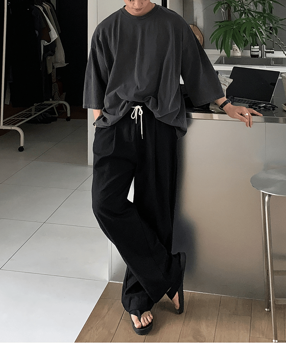 ダークグレーのオーバーサイズTシャツにブラックのワイドイージーパンツ、サンダルを合わせた人物の全身スタイリング写真。