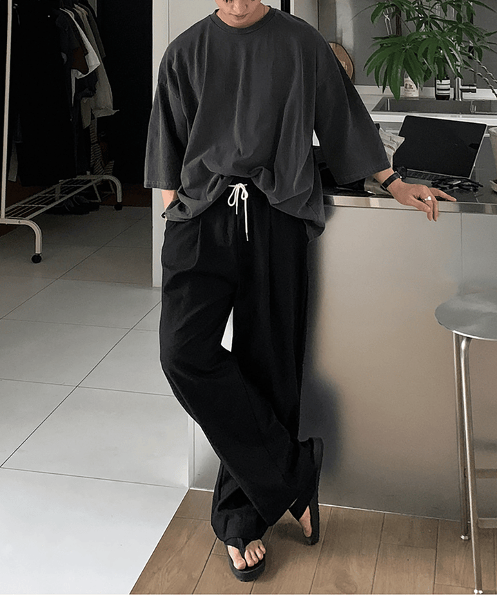 ダークグレーのオーバーサイズTシャツにブラックのワイドイージーパンツ、サンダルを合わせた人物の全身スタイリング写真。
