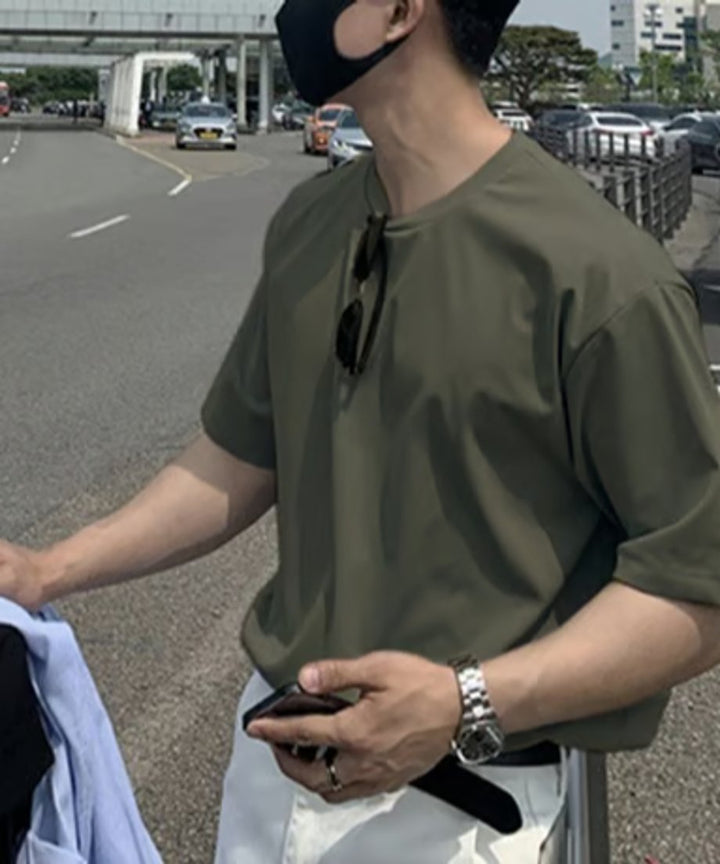 アーミーグリーンのクルーネックTシャツにサングラスを掛け、ホワイトのボトムスを合わせた男性を横から捉えたカット。