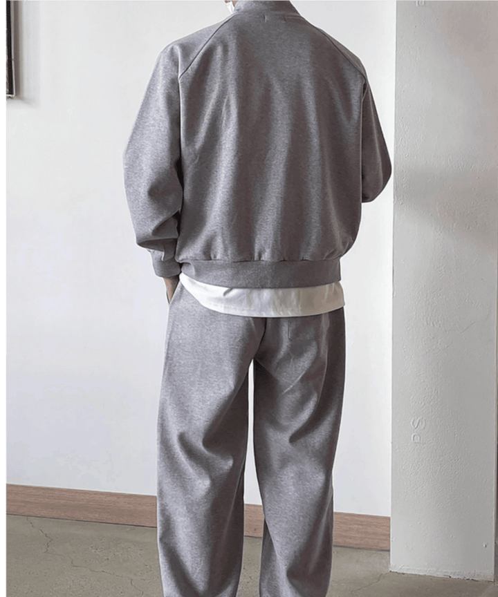 グレーのジップアップジャケットとパンツのセットアップを着用した男性の、すっきりとした後ろ姿の全身ショット