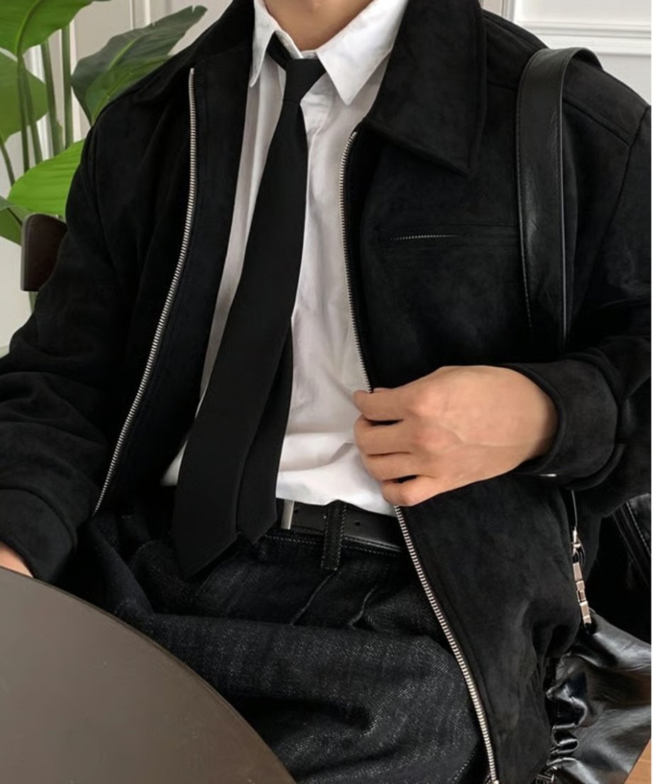 黒いレザートートバッグを肩に掛け、ブラックのフェイクスエードブルゾンの裾を軽く手で整える男性の胸元のクローズアップ