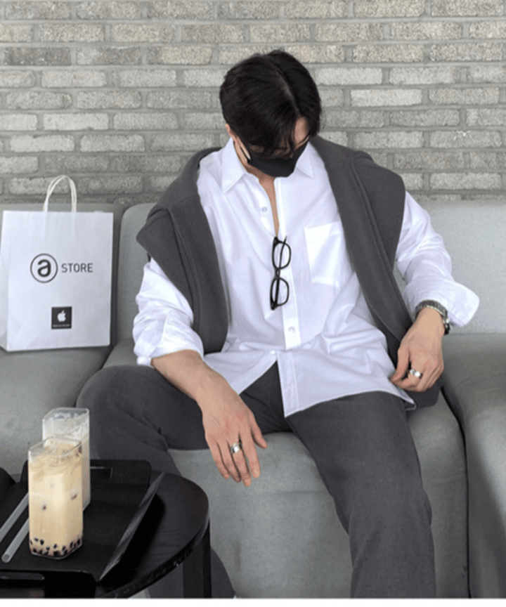 ホワイトのシャツにグレーのニットを肩掛けし、グレーのパンツを合わせてソファに座りながら、テーブルの上のタピオカドリンクを見つめている男性の俯瞰カット。