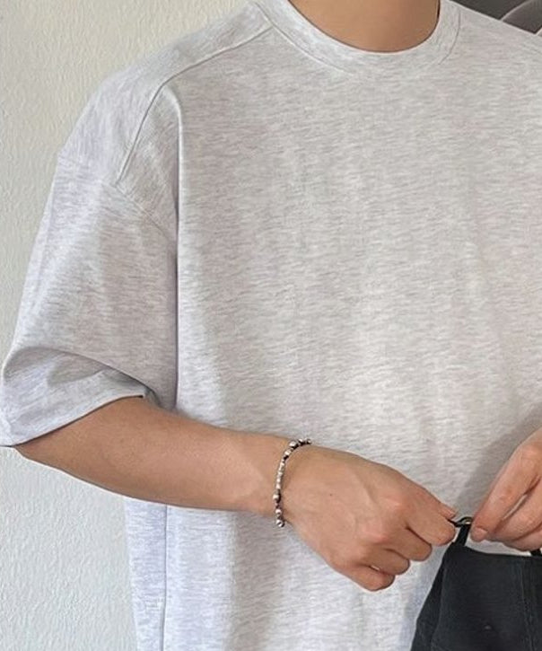 ホワイトのルーズTシャツに黒のスラックス、ブラウンのレザーバンドの腕時計を合わせたカット。