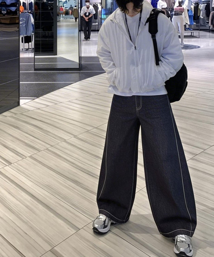 ダークブルーのワイドバギーデニムパンツにスリッポンスニーカーを合わせてやや斜めを向いて立っている、ルーズなサイズ感が伝わるコーディネート写真。