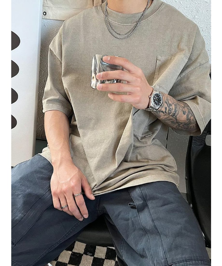 オーバーサイズのポケットTシャツを着用した男性が、グラスを片手にリラックスした佇まいで佇む、日常のストリートモードなスタイリングをイメージしたカット。