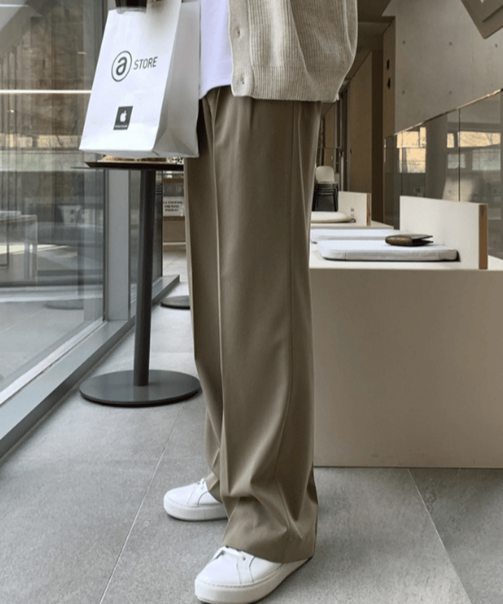 アイボリーのカーディガンの下から覗く、美しい落ち感とセンタープレスが際立つダークベージュのワイドストレートパンツの側面アップ。