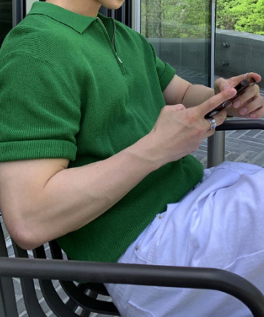 鮮やかなグリーンのハーフジップニットポロを着用し、椅子に座ってスマートフォンを操作する男性の手元・腕元のクローズアップカット。