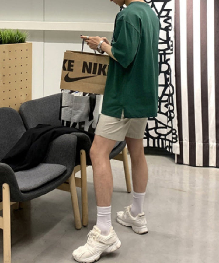 ダークグリーンのロゴTシャツにハーフパンツ、白ソックスと白スニーカーを合わせた男性の全身の立ち姿