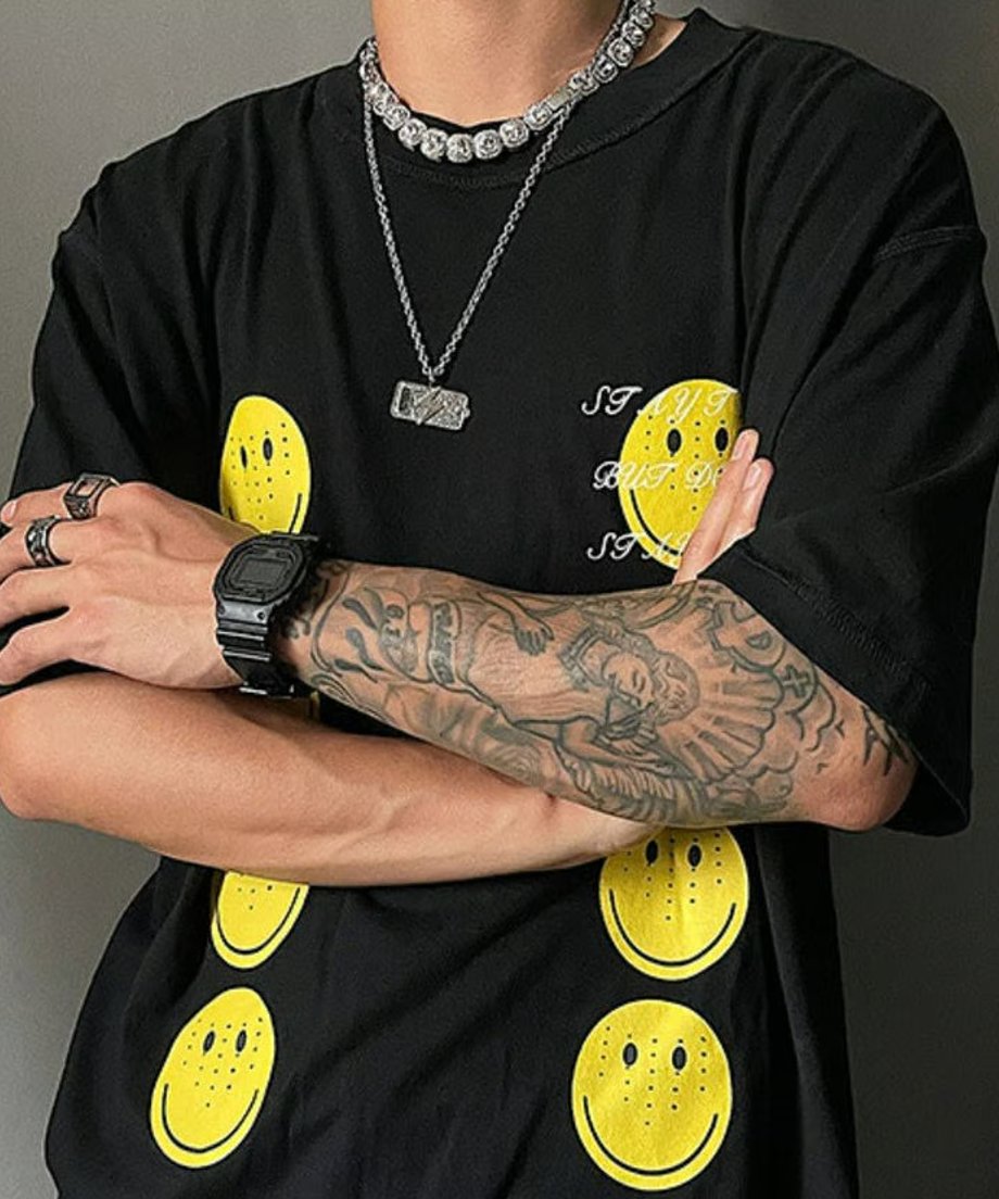 スマイルプリントの黒Tシャツを着用し、両腕を組んだストリートモードな雰囲気のメンズコーディネートカット。